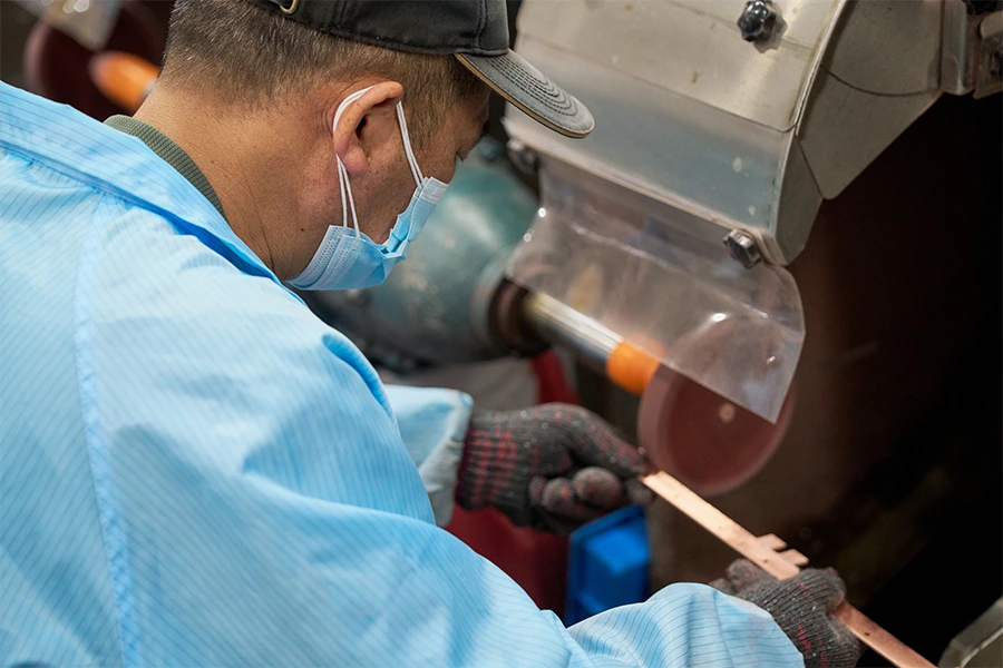 Worker cutting copper bar at a saw station